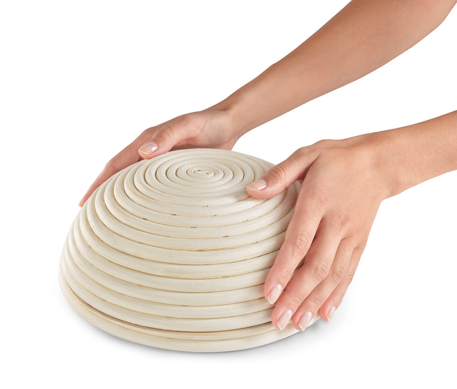 İki el yuvarlak bir mayalama sepetini tutuyor.