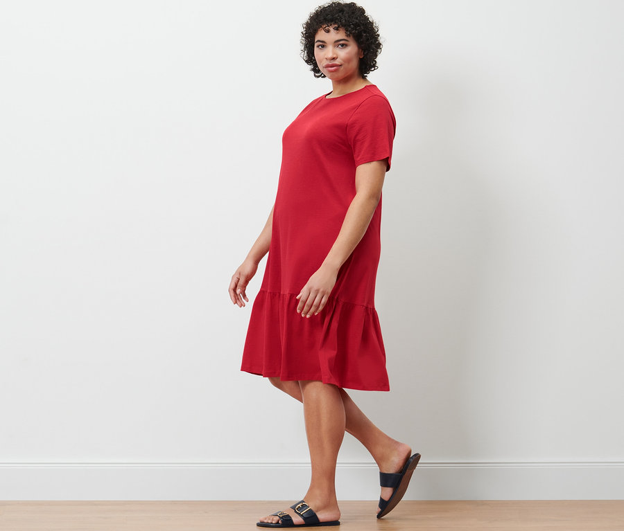 Kadın yürüyor ve kırmızı organik pamuklu volanlı jarse elbise giyiyor.