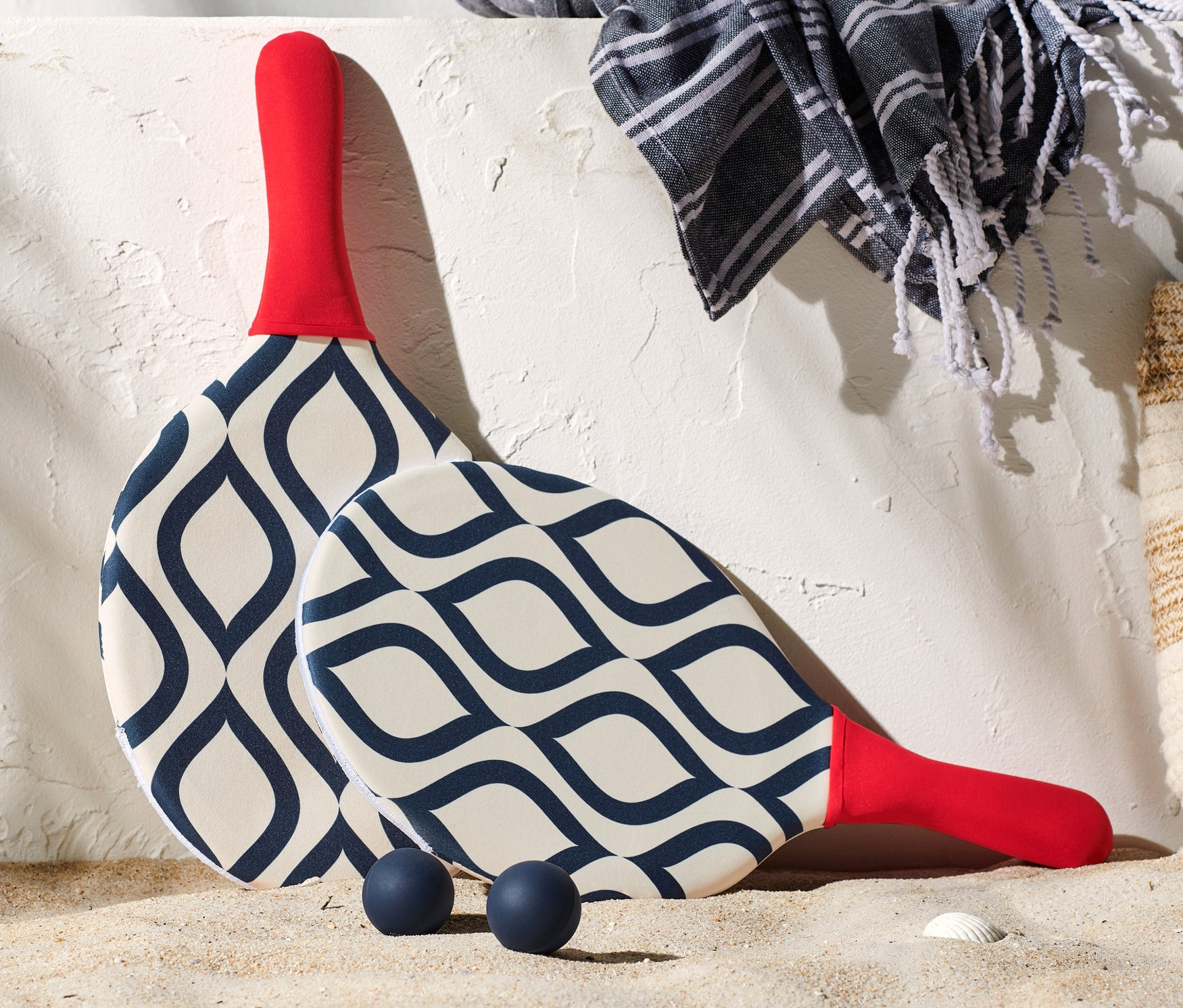 Plaj topu seti, bir çanta, havlu ve güneş kremi yanında kumda duruyor.