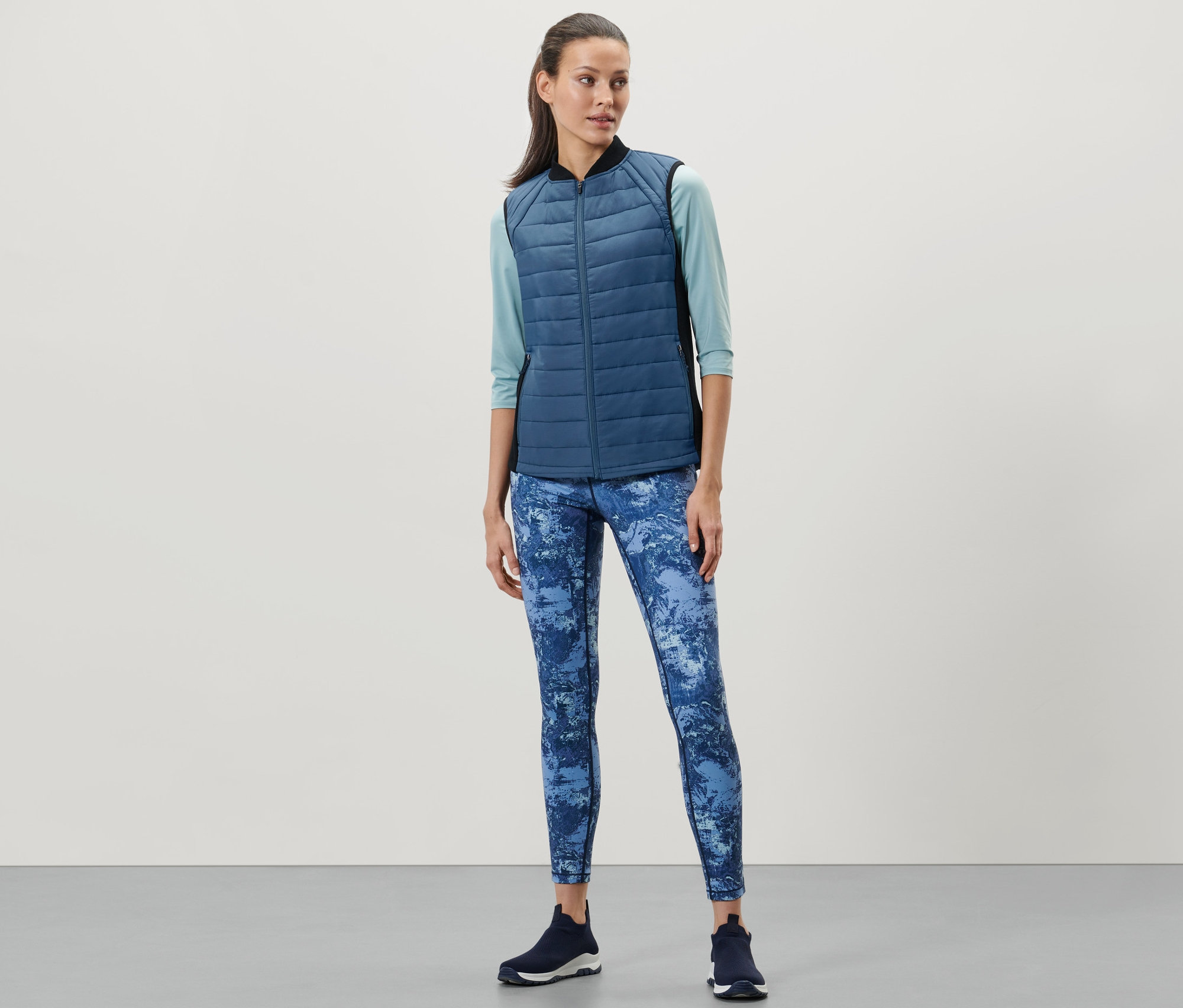 Kadın, Termal Kapitone Yelek, mavi tayt ve koyu renk spor ayakkabı giyiyor.