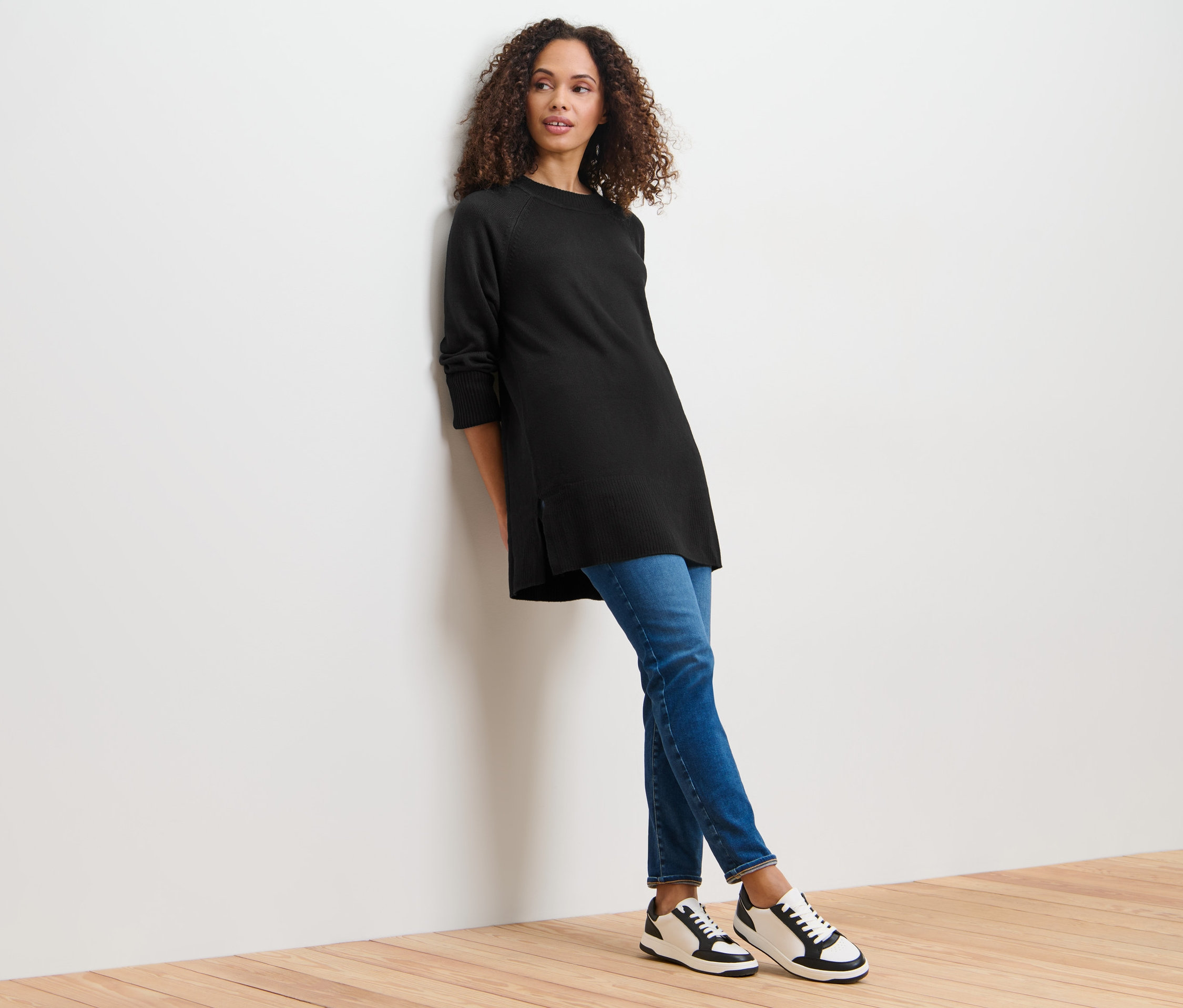 Duvara yaslanmış, uzun siyah örgü kazağı olan kadın.