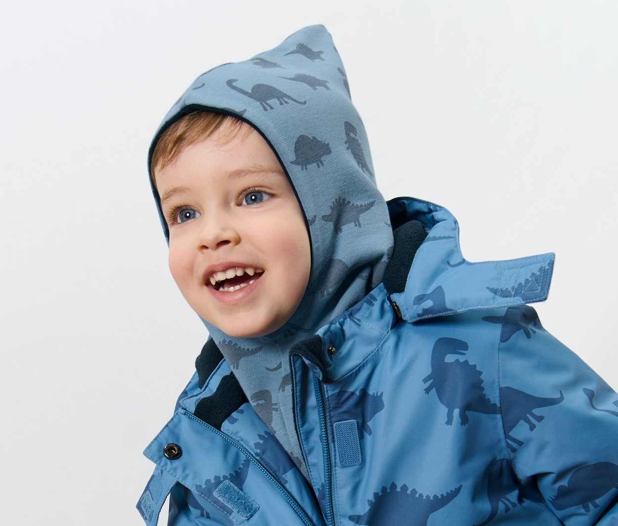 Dinozor desenli çocuk boyunluklu çift taraflı bere ve dinozor desenli mont giyen bir erkek çocuk.