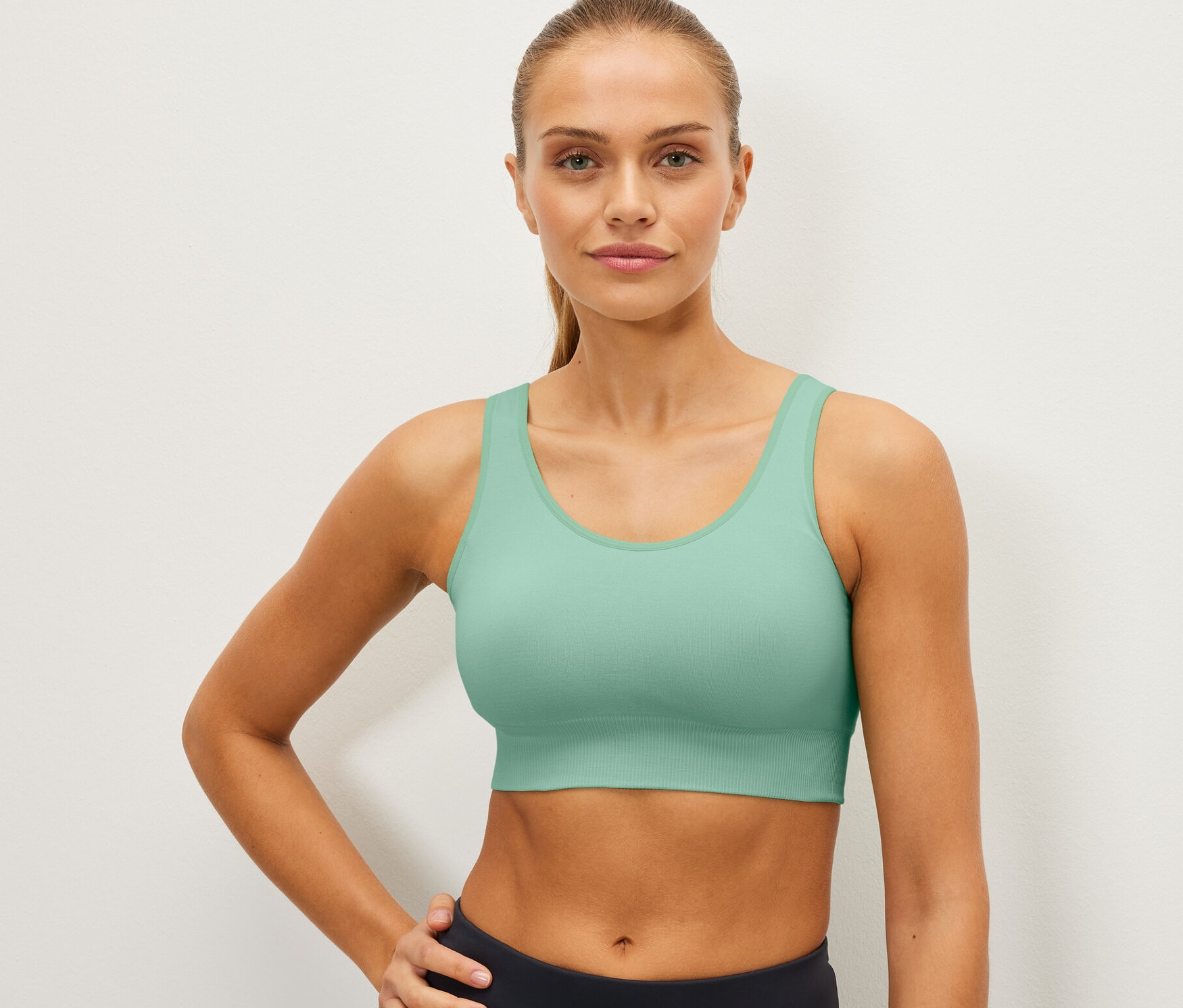 Kadın nane yeşili dikişsiz spor büstiyer ile poz veriyor.