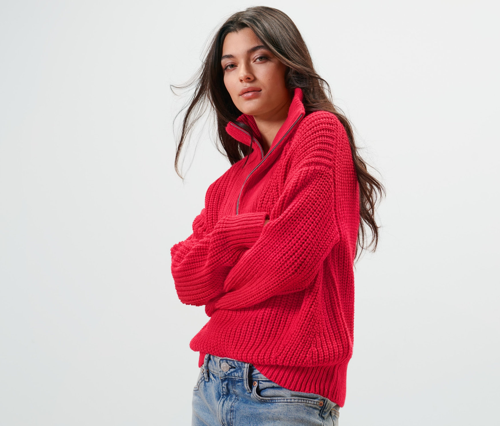 Kadın kırmızı kalın örgü troyer kazak ve kot pantolon giyiyor.