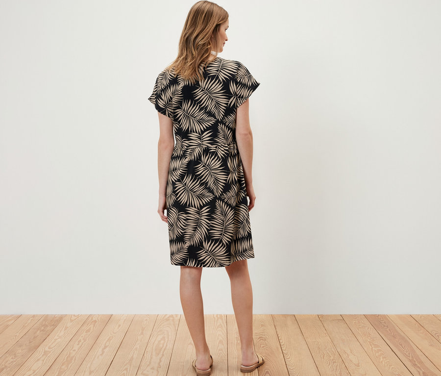 Bir kadın kameraya arkası dönük duruyor ve baskılı bir jarse elbise giyiyor.