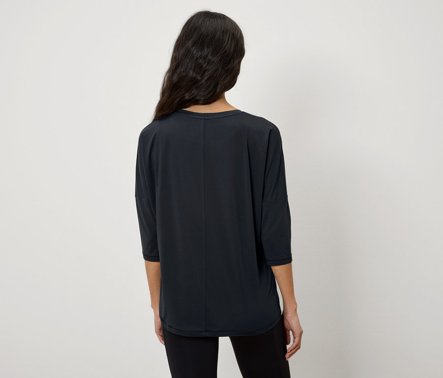 Kameraya arkası dönük bir kadın, üç çeyrek kollu siyah bir tişört giyiyor.