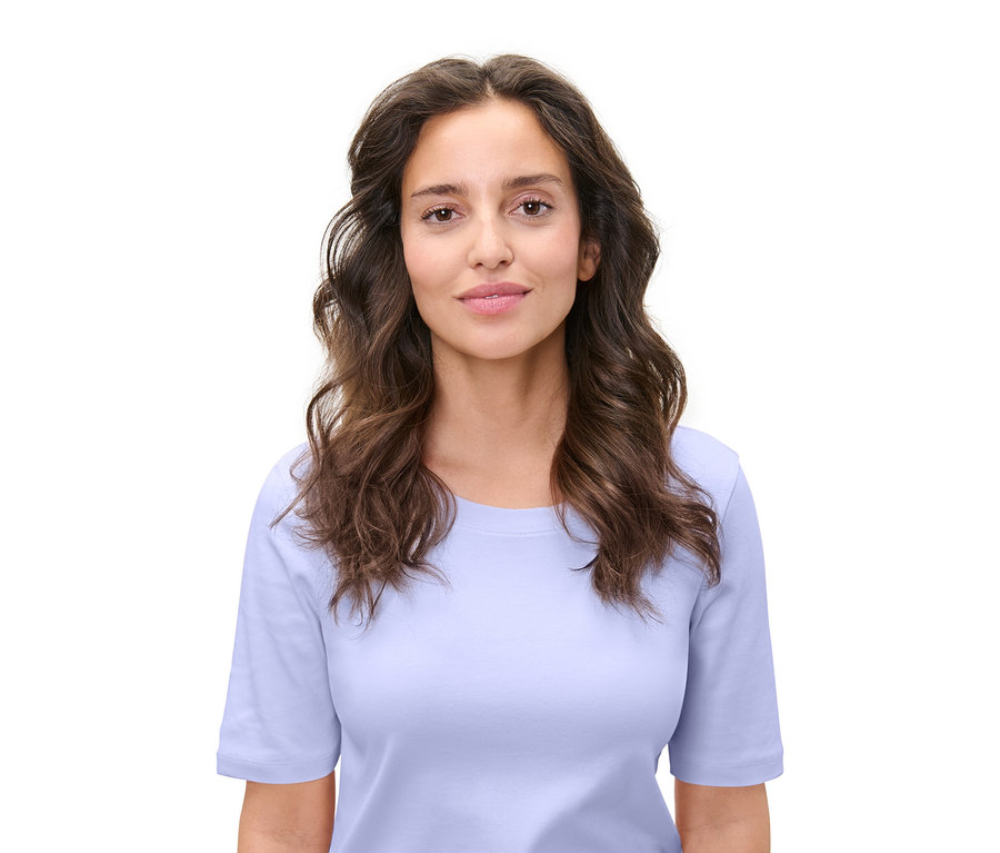 Beyaz bir arka plan üzerinde açık mavi bir tişört giyen kahverengi dalgalı saçlı bir kadının portresi.