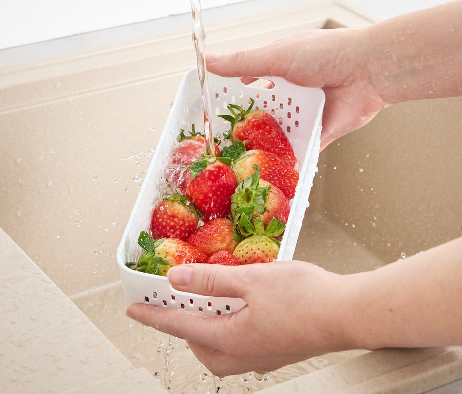 Bir kişi lavaboda çilekleri süzgeçli bir saklama kabında yıkıyor.