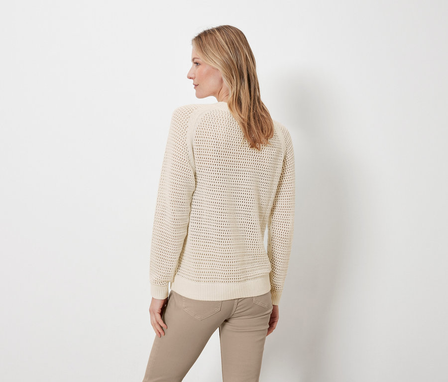 Bir kadın kameraya arkası dönük poz veriyor, üzerinde krem rengi pointelle örgü kazak ve bej pantolon var.