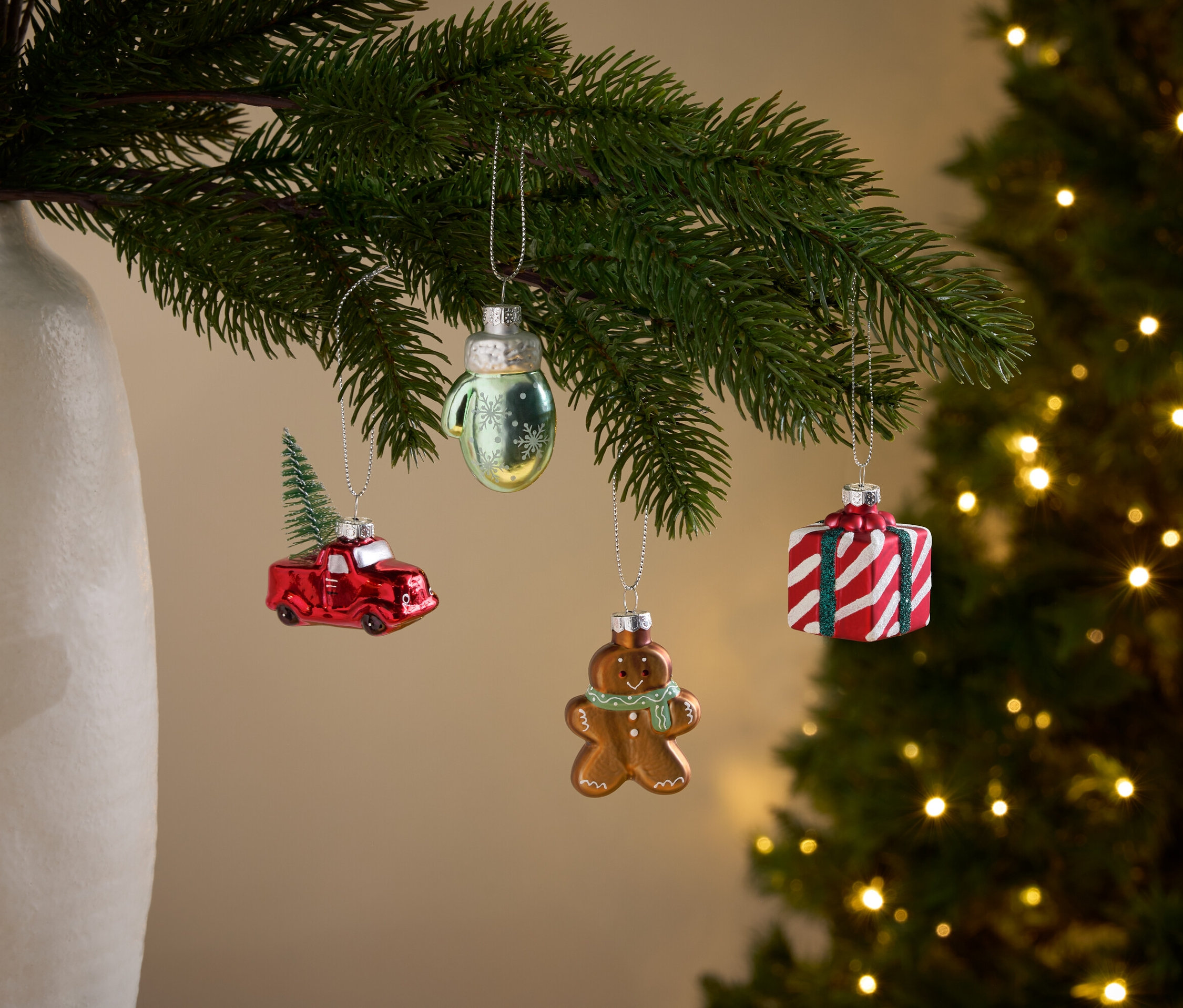 Noel ağacı dalları üzerinde kırmızı araba, eldiven, zencefilli kurabiye adam ve hediye şeklinde süslemeler asılı duruyor.
