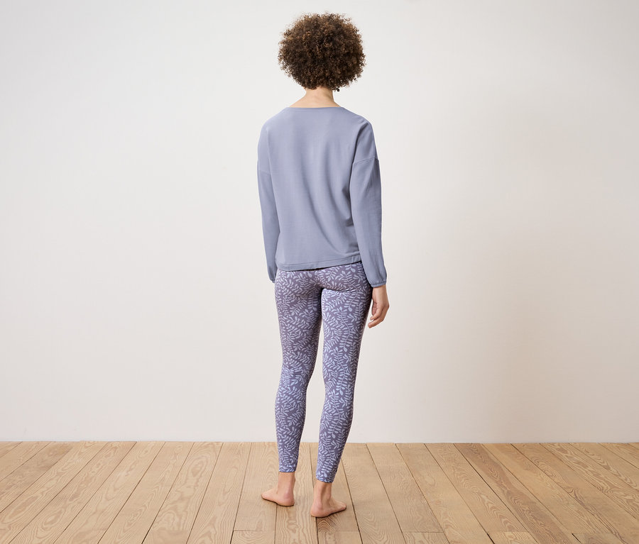 Arkası dönük bir kadın mavi uzun kollu bir bluz ve desenli bir tayt giyiyor.