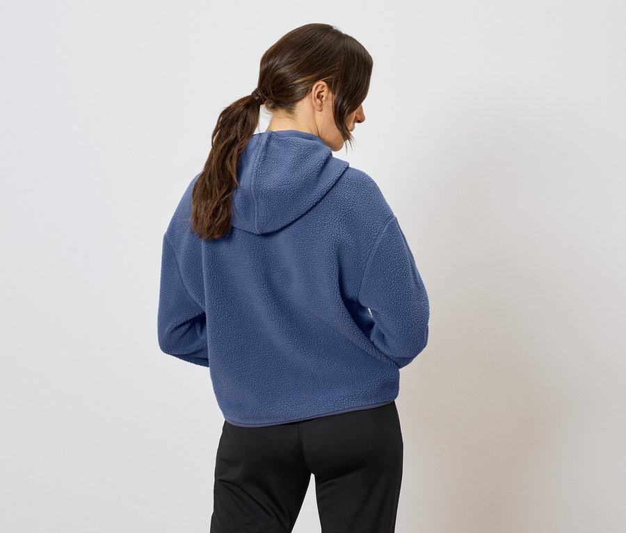 Kahverengi saçları at kuyruğu yapılmış, mavi kapüşonlu bir sweatshirt ve siyah pantolon giyen bir kadının arka görüntüsü.