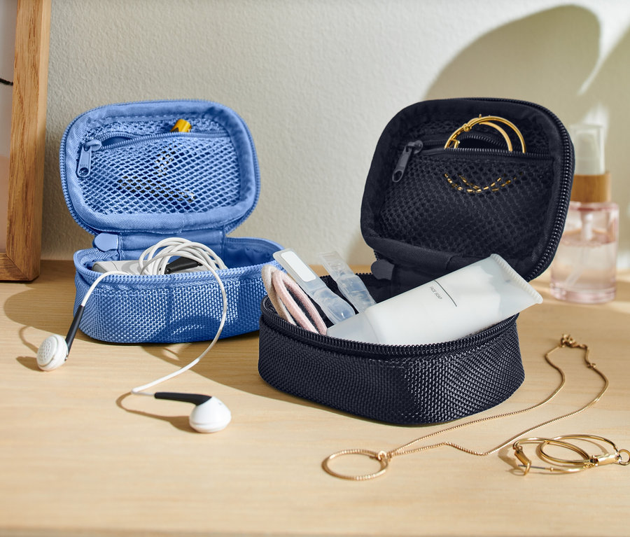 Bir masa üzerinde açık halde iki küçük saklama çantası duruyor; biri mavi renkli ve içinde kulaklıklar var, diğeri ise koyu renkli ve içinde cilt bakım ürünleri ve takılar bulunuyor.