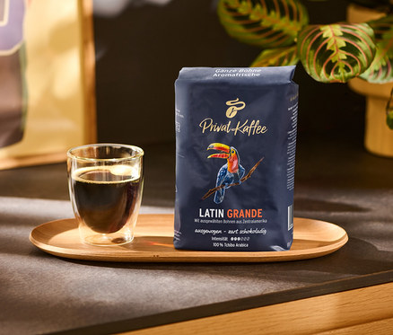 Bir fincan kahve ve tahta bir tepsi üzerinde bir paket Privat Kaffee Latin Grande - 500 g Çekirdek Kahve.