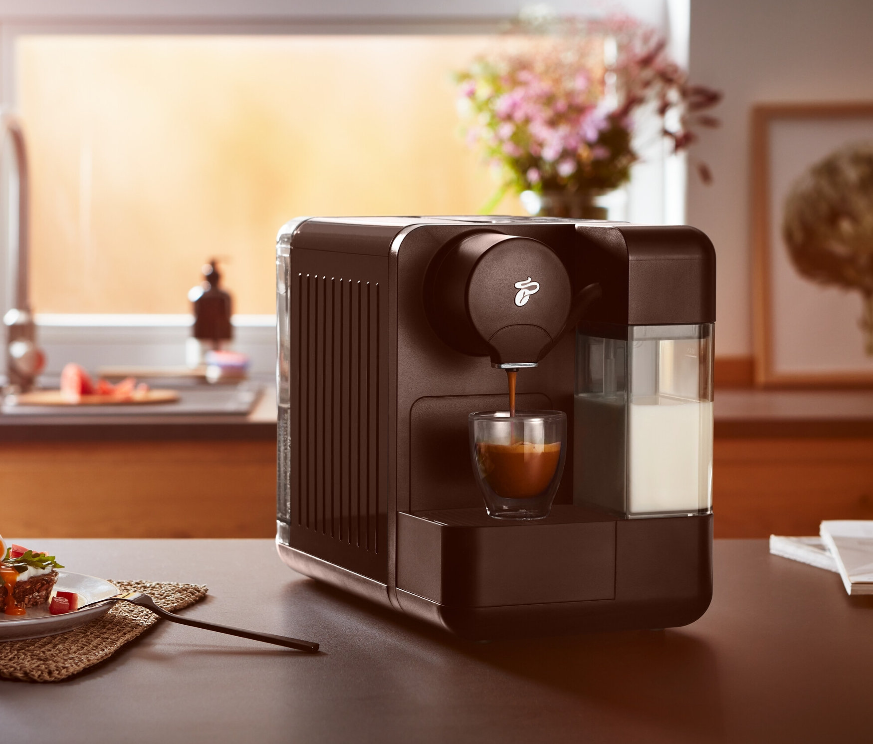 Siyah Cafissimo milk, bir bardağa kahve hazırlıyor. Masanın üzerinde yemek olan bir tabak var.