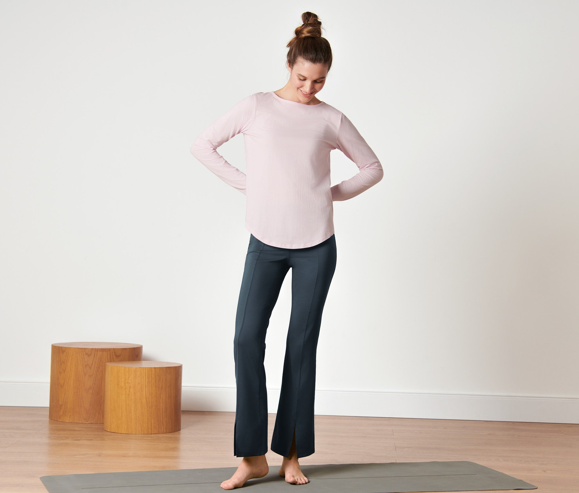 Kadın yoga matının üzerinde duruyor ve koyu mavi renkli Bodyforming Spor Pantolon giyiyor.