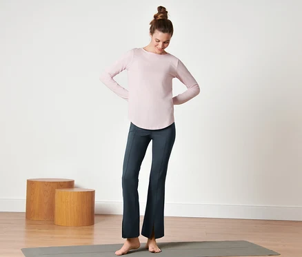 Kadın yoga matının üzerinde duruyor ve koyu mavi renkli Bodyforming Spor Pantolon giyiyor.