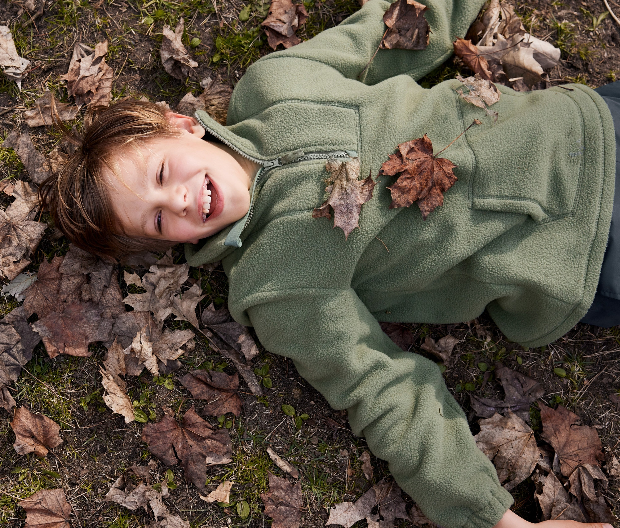 Zeytin yeşili Yumuşa Polar Sweatshirt giyen gülümseyen bir çocuk yerde yatıyor.