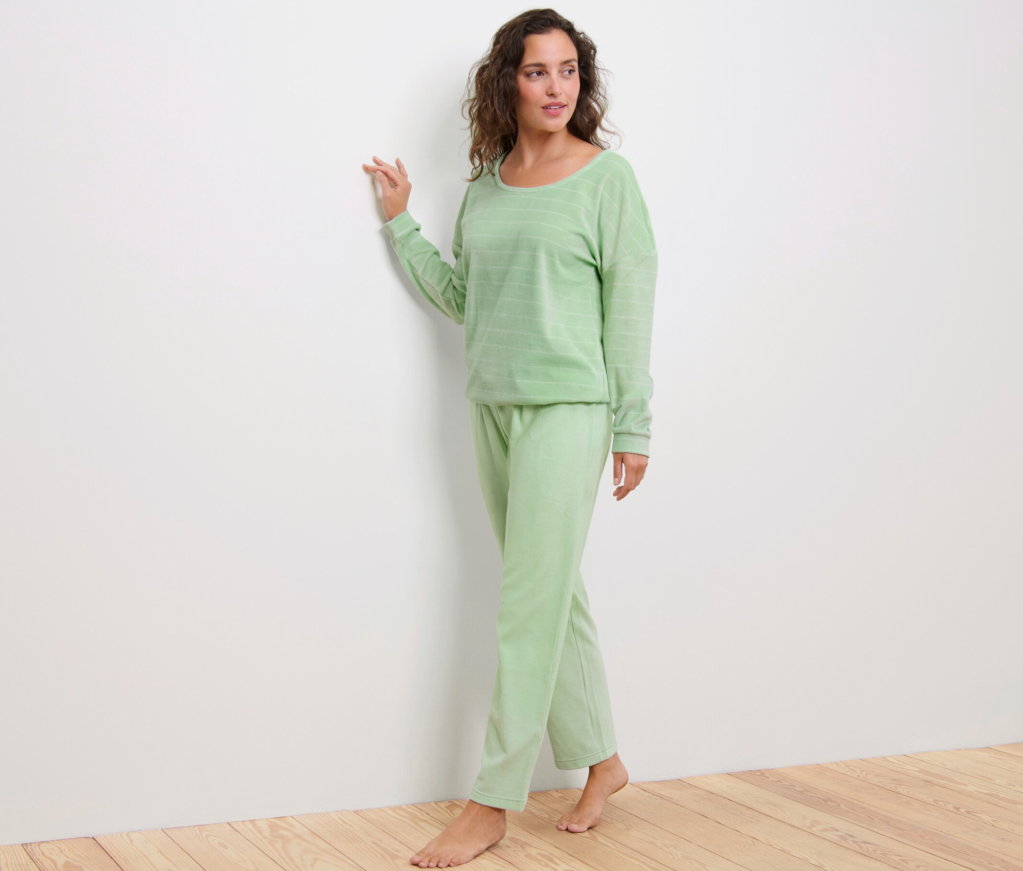 Kadın ayakta duruyor ve yeşil niki pijama takımı giyiyor.