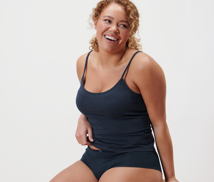 Bir kadın taburede oturuyor ve 2'li atlet setinden mavi bir atlet giyiyor.