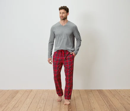 Gri uzun kollu tişört ve kırmızı ekose pijama altı giyen bir adam ahşap zeminde duruyor.