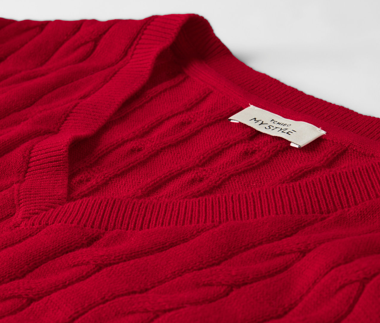 Yakın çekimde, kırmızı renkli, örgü desenli bir kazağın yaka kısmında etiketi bulunuyor.