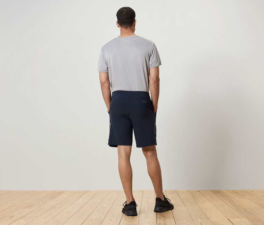 Sırtı kameraya dönük bir adam gri tişört, lacivert şort ve siyah spor ayakkabı giyiyor.