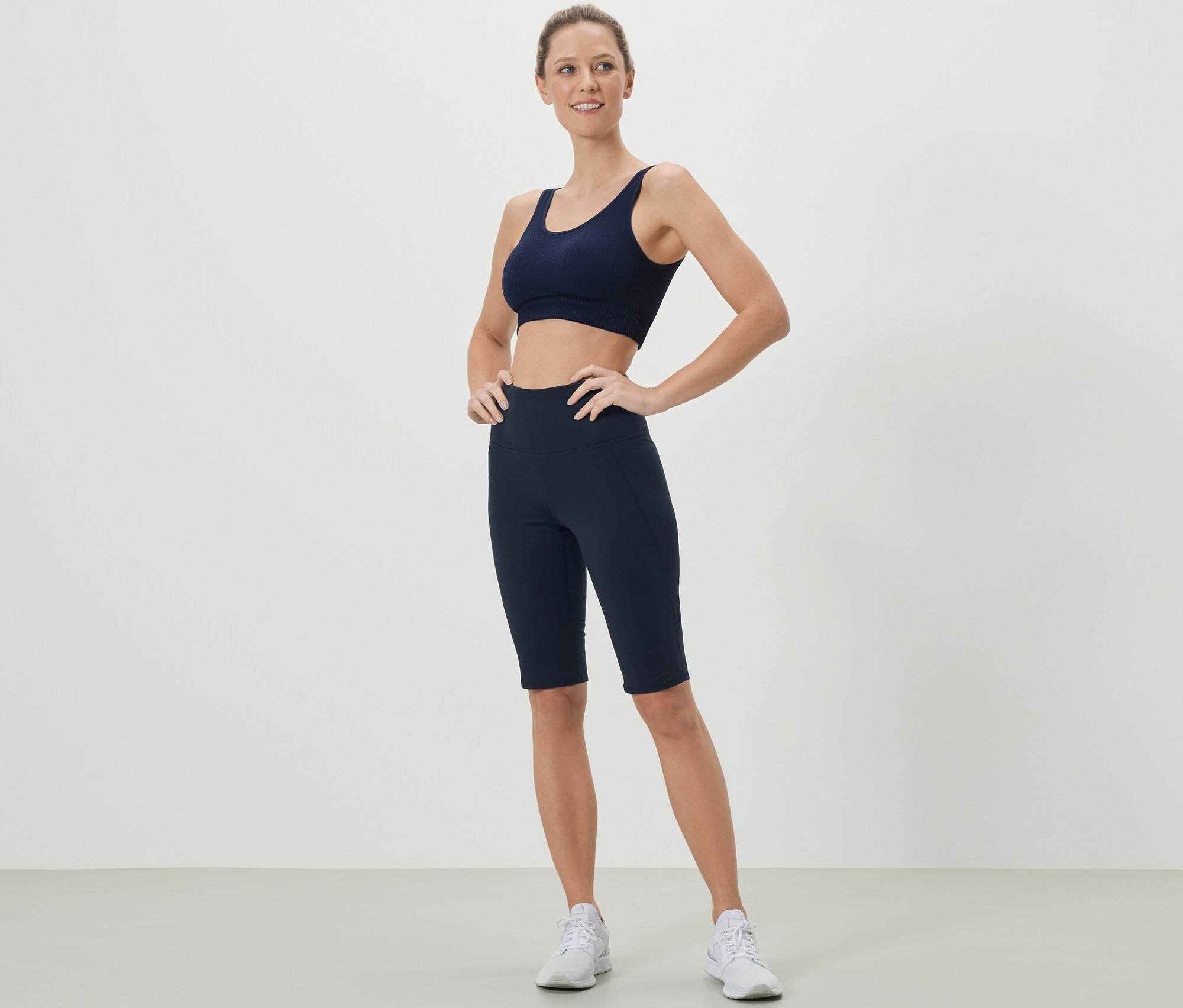 Kadın lacivert spor sütyeni ve bisikletçi taytıyla poz veriyor.