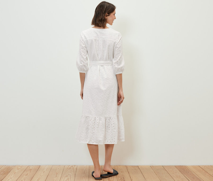 Kadın kameraya arkası dönük duruyor ve brodeli bluz elbise giyiyor.