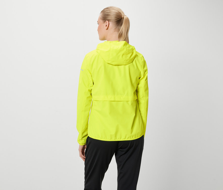 Arkadan, sarı saçları at kuyruğu yapılmış bir kadın, neon sarısı kapüşonlu bir ceket ve siyah pantolon giyiyor.