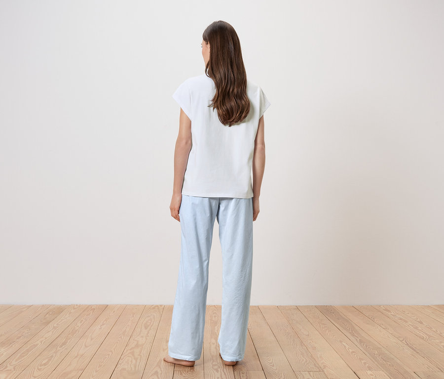 Kadın sırtı kameraya dönük, beyaz tişört ve açık mavi pijama altı giyiyor.
