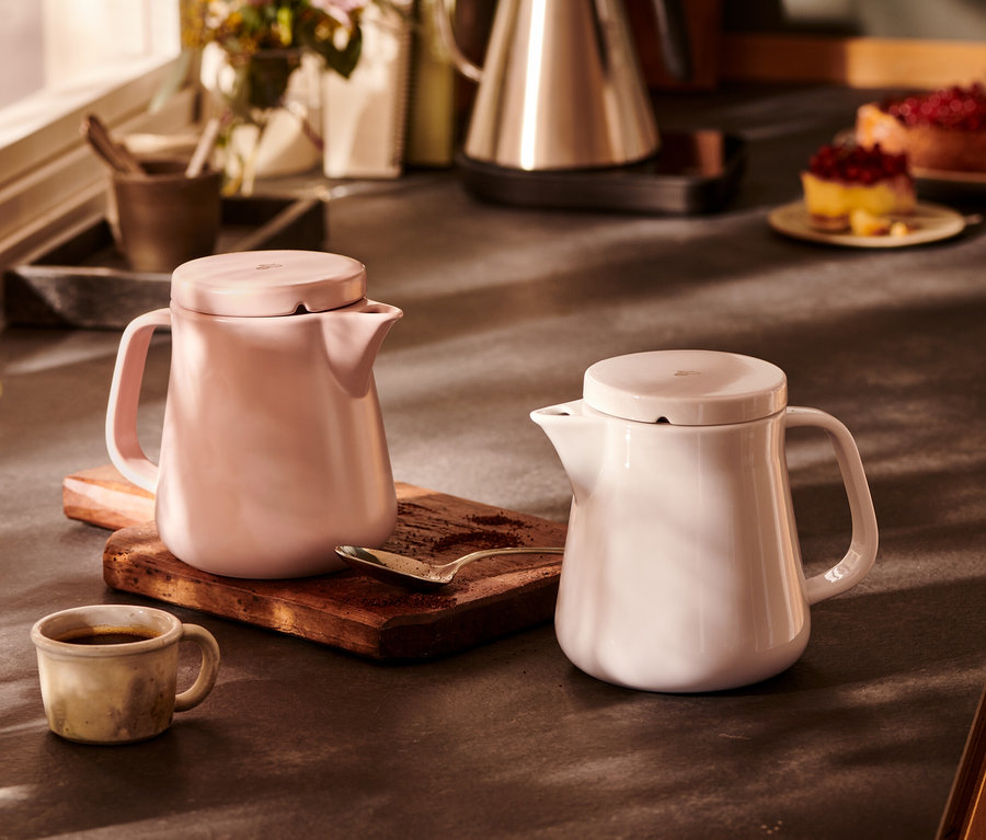Ahşap bir tahta üzerinde yan yana duran iki seramik Kaffeebereiter, beyaz ve pembe. 