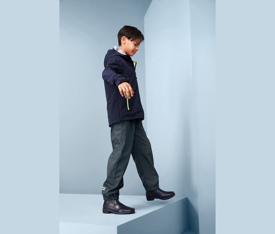 Bir çocuk merdivenden yukarı çıkıyor, üzerinde jean görünümlü softshell pantolon, ceket ve botlar var.