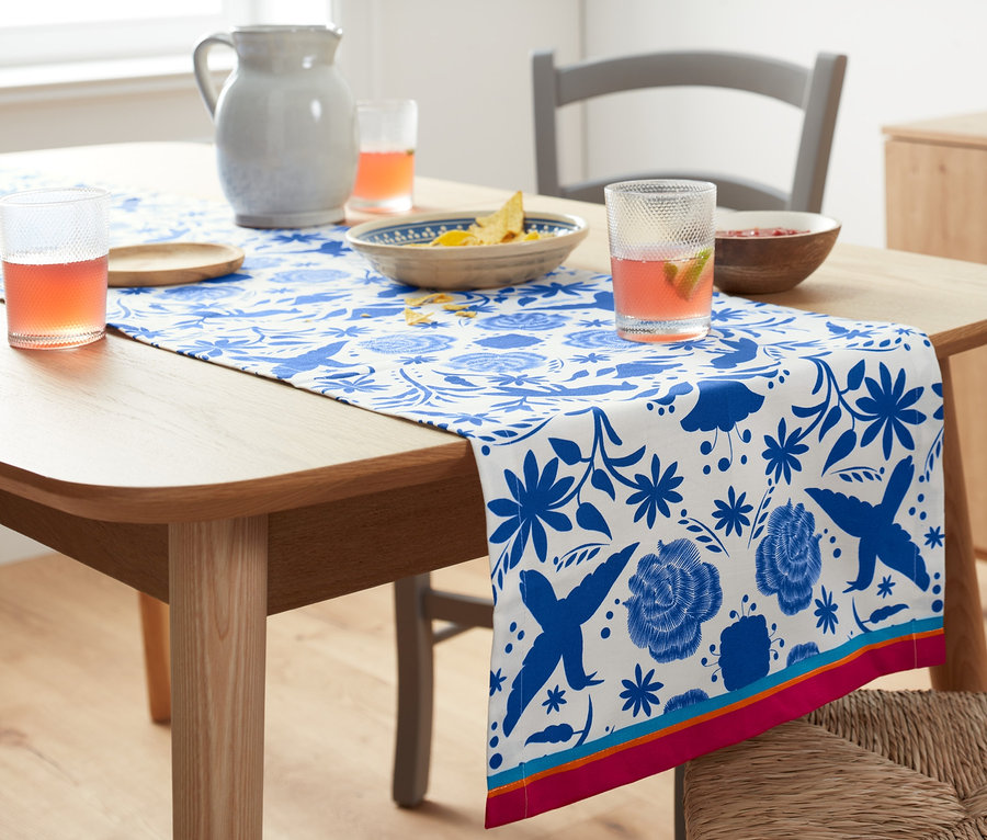Masanın üzerinde mavi çiçek desenli organik pamuklu şerit örtü var. Masanın üzerinde içecekler ve atıştırmalıklar var.