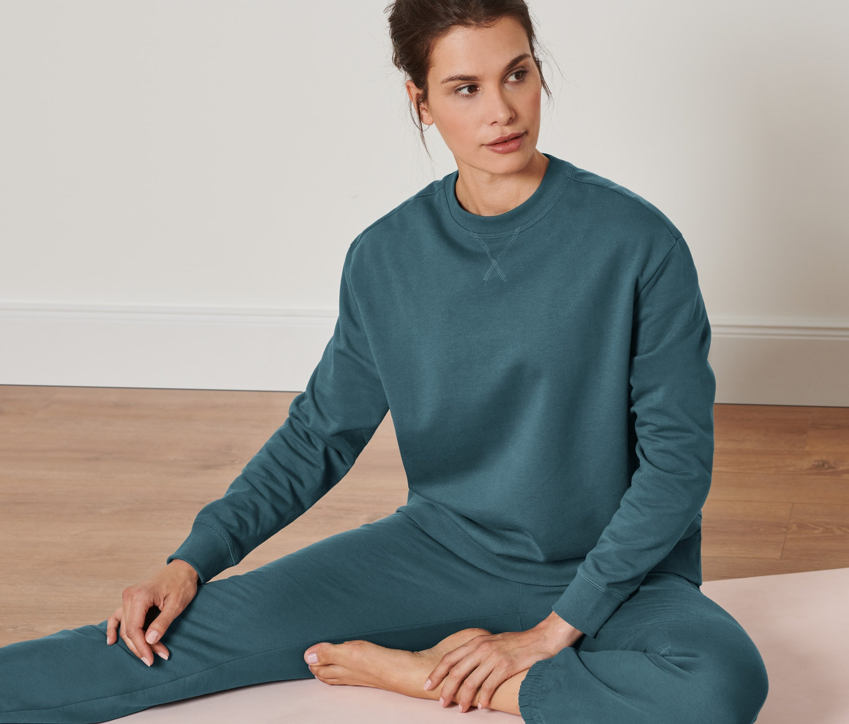 Bir kadın yoga matında oturuyor ve Oversize Yoga Sweatshirt, Koyu Zümrüt Yeşili renginde bir sweatshirt giyiyor.