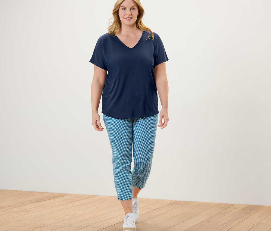 Kadın yürüyor ve Tamamı Baskılı 7/8 Streç Pantolon, V yaka tişört ve spor ayakkabı giyiyor.