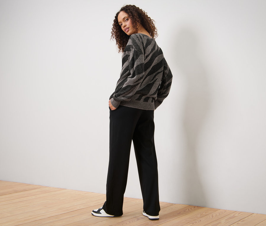 Kadın Jakarlı Örgü Kazak, siyah pantolon ve spor ayakkabılarıyla poz veriyor.