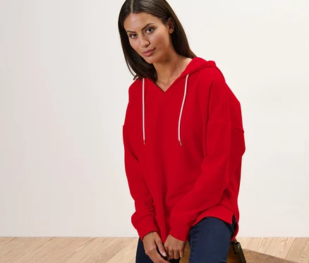 Kadın sandalyede oturuyor ve kırmızı bir kapüşonlu sweatshirt giyiyor.