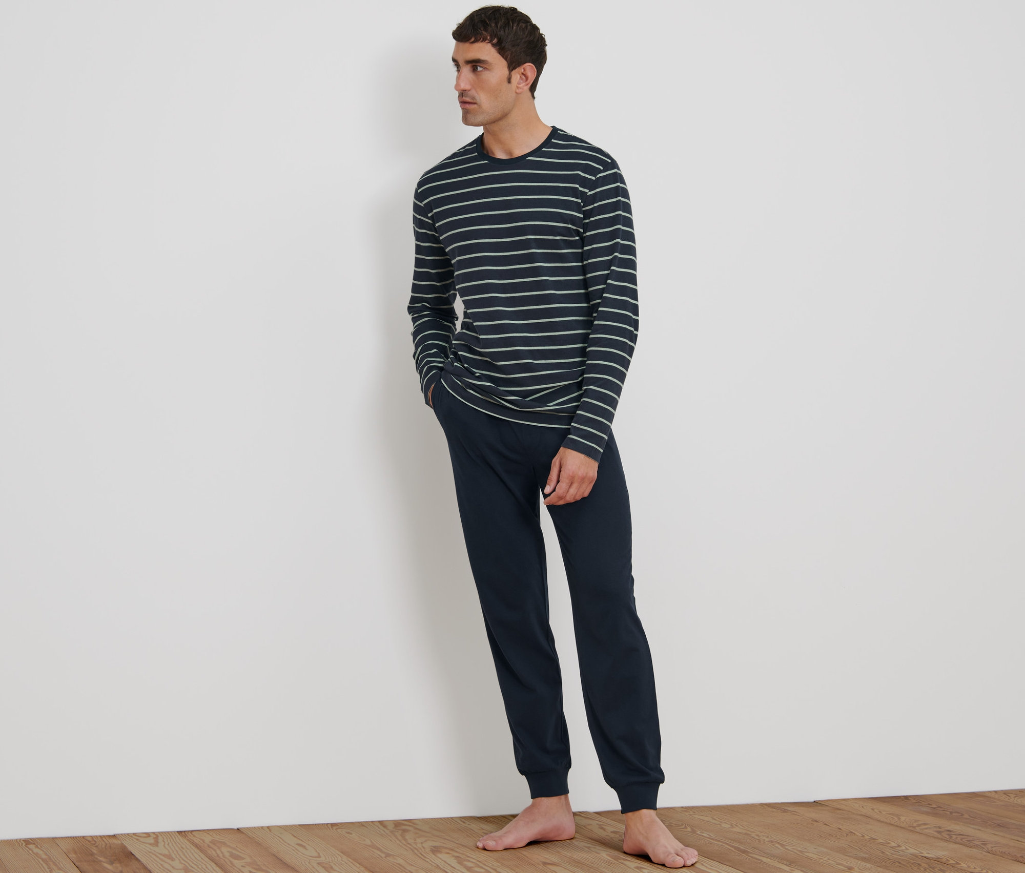 Çizgili üst ve lacivert pantolonlu pijamalı bir adam duvara yaslanmış.