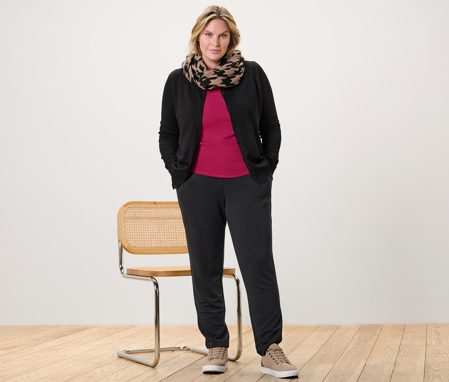 Kadın, vişne rengi 3/4 kollu tişört, ince örgü hırka ve jogger pantolonla poz veriyor.