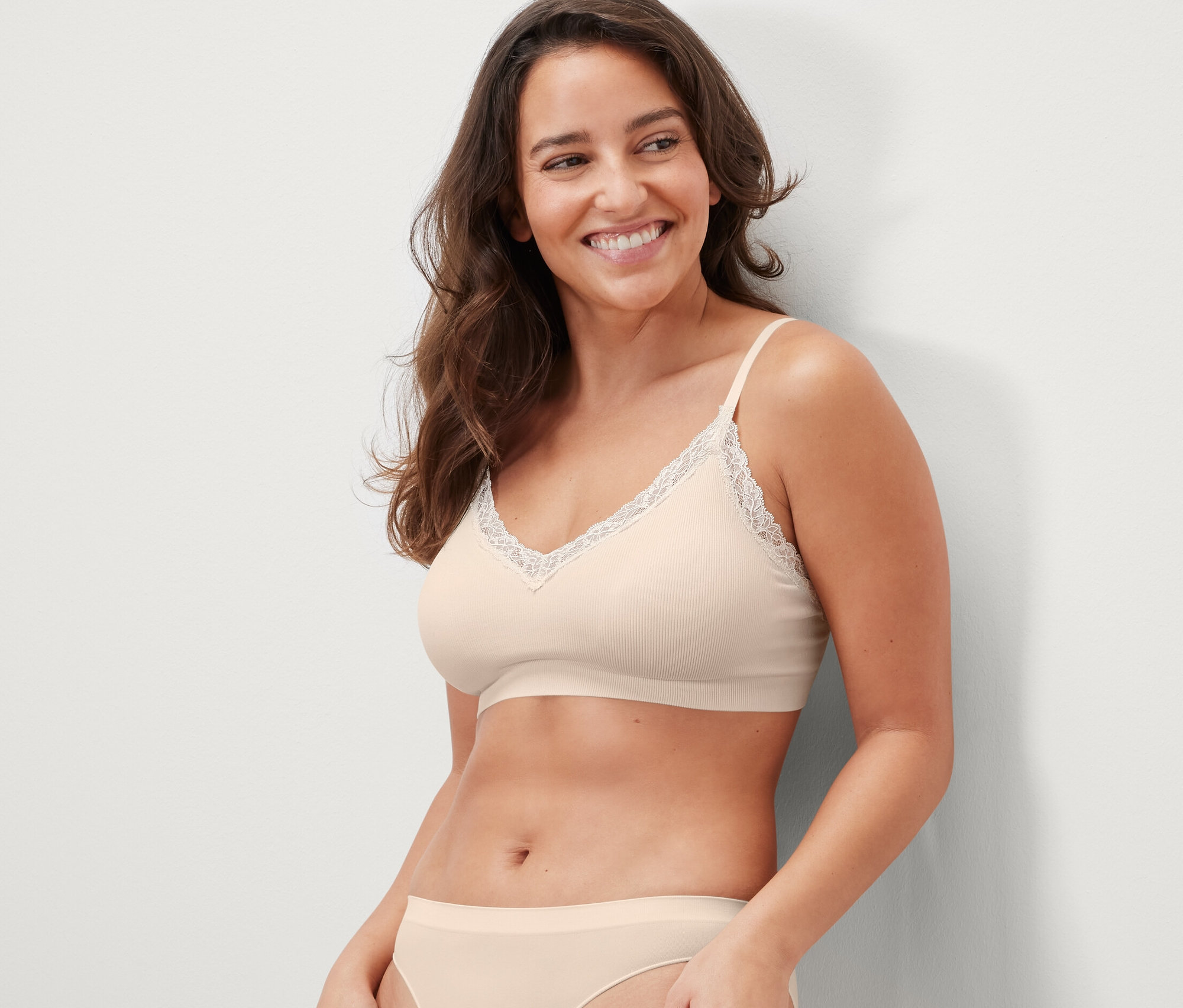 Gülümseyen bir kadın krem rengi, dantelli, dikişsiz bir büstiyer giyiyor.