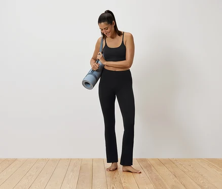 Siyah spor kıyafetli bir kadın yoga matı tutuyor.
