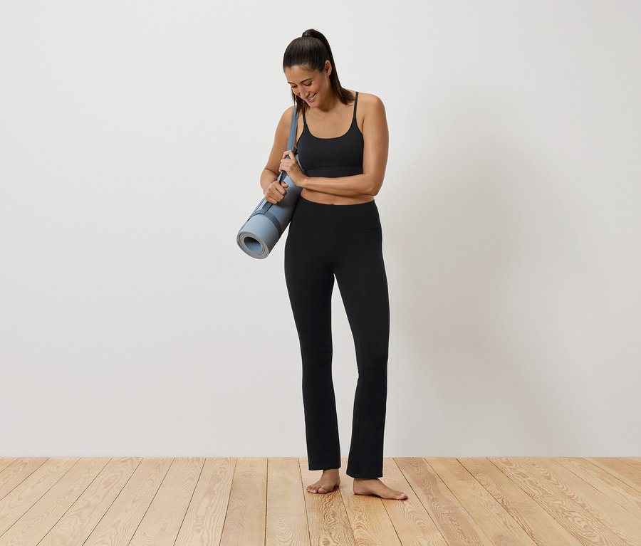 Siyah spor kıyafetli bir kadın yoga matı tutuyor.