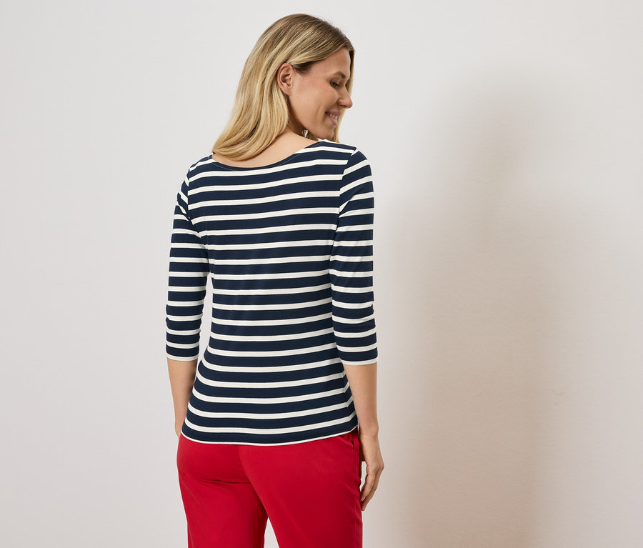 Sarışın bir kadın, lacivert ve beyaz çizgili bir tişört ve kırmızı pantolon giyiyor.