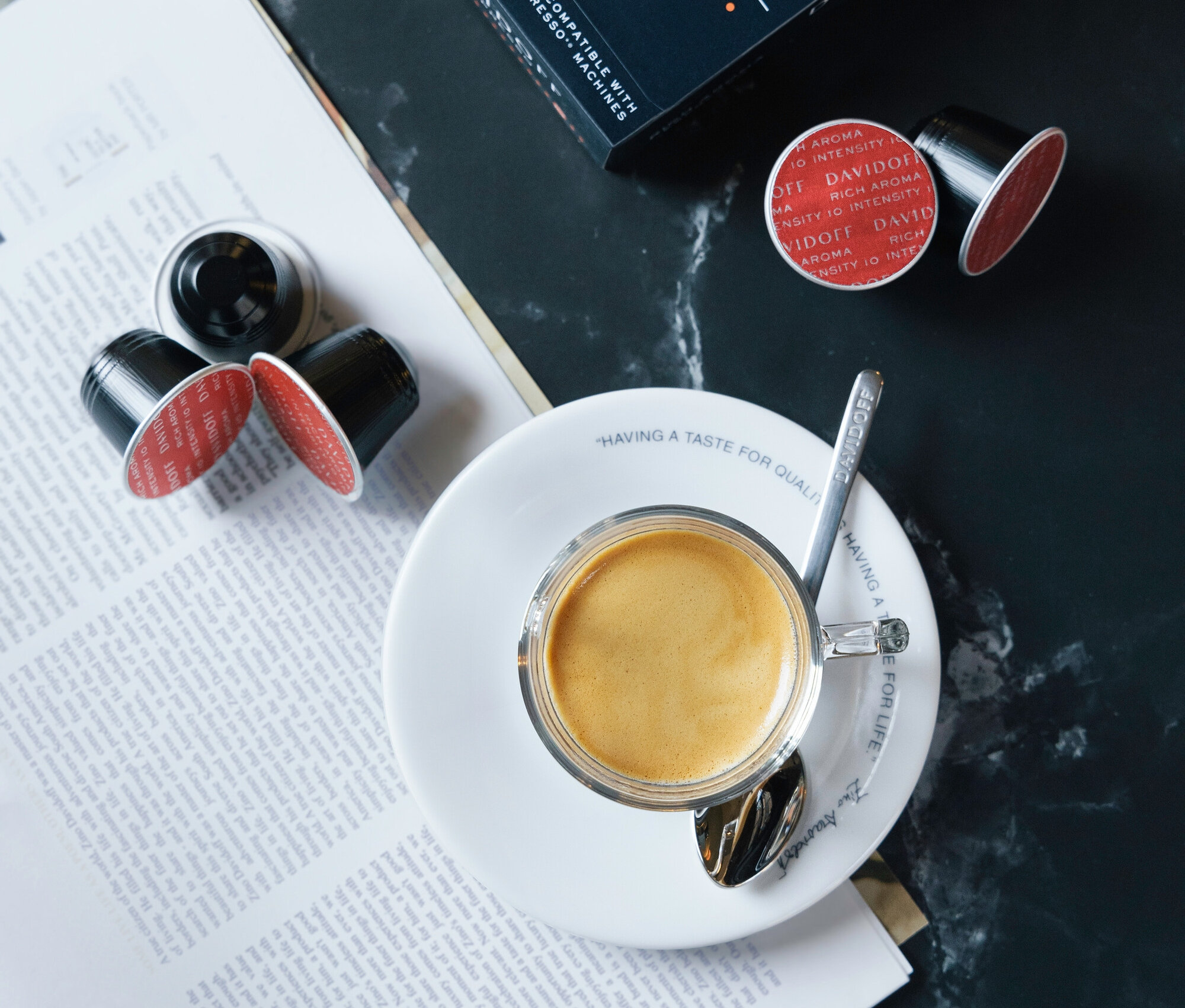 DAVIDOFF CAFÉ Rich Aroma paketinin ve kahve kapsüllerinin yanında kaşıklı fincan içinde espresso.