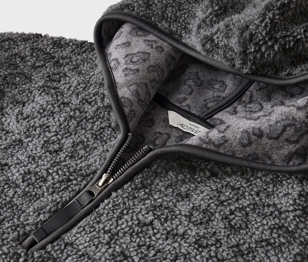 Kapüşonun iç kısmında gri hayvan deseni bulunan, fermuarlı, gri, tüylü bir kapüşonlu sweatshirt'ün detay görüntüsü.