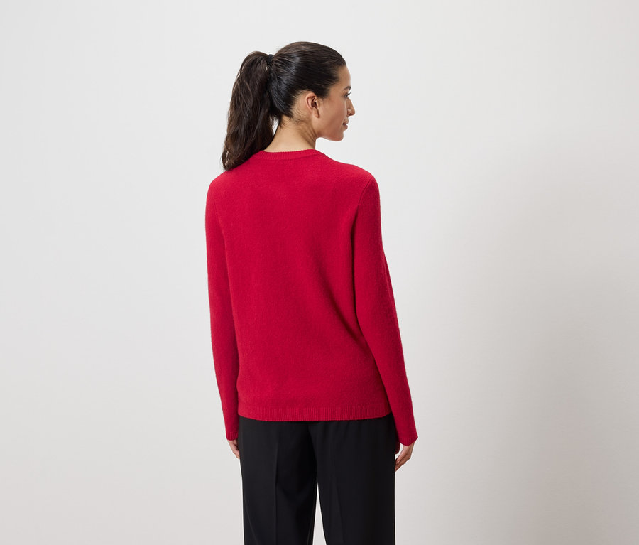 Sırtı kameraya dönük bir kadın kırmızı bir kazak ve siyah pantolon giyiyor.