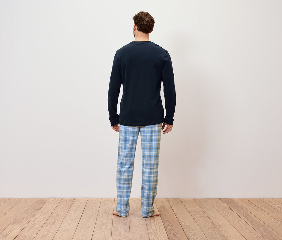 Arkası dönük bir adam mavi uzun kollu bir pijama ve mavi kareli bir pantolon giyiyor.
