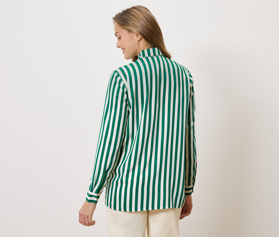 Arkadan görünen, yeşil beyaz çizgili bir bluz ve bej pantolon giyen bir kadın.