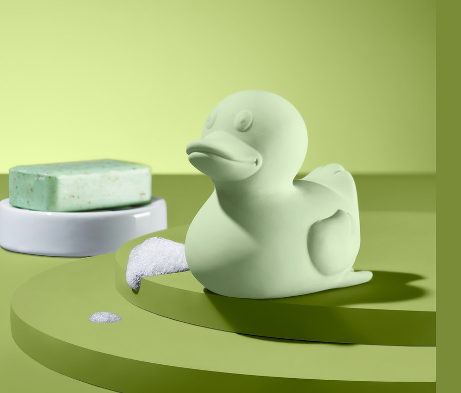 Yeşil renkli küçük bir banyo ördeği ve beyaz bir stand üzerinde yeşil sabun.